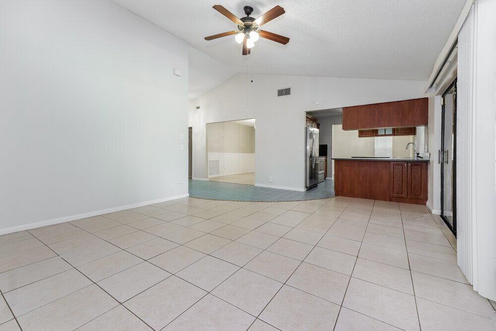 A spacious living area features light-colored floor tiles, a vaulted ceiling, and a ceiling fan — WELLINGTON, FL