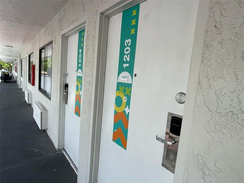 An exterior view shows two hotel-style doors numbered 1203 and 1204 with colorful vertical decals — 5367 W IRLO BRONSON MEM HWY UNIT 1-203, KISSIMMEE, FL
