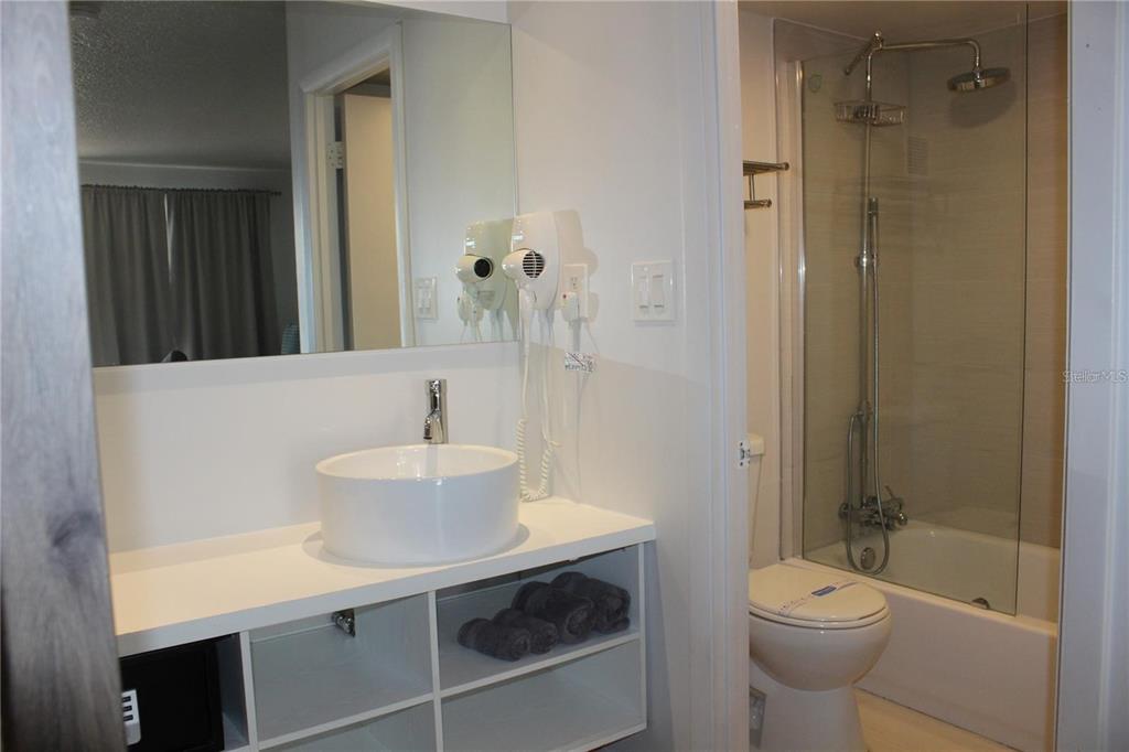 A bathroom features a white vessel sink, open shelving, and a glass-enclosed shower-tub combination — 5367 W IRLO BRONSON MEM HWY UNIT 1-203, KISSIMMEE, FL