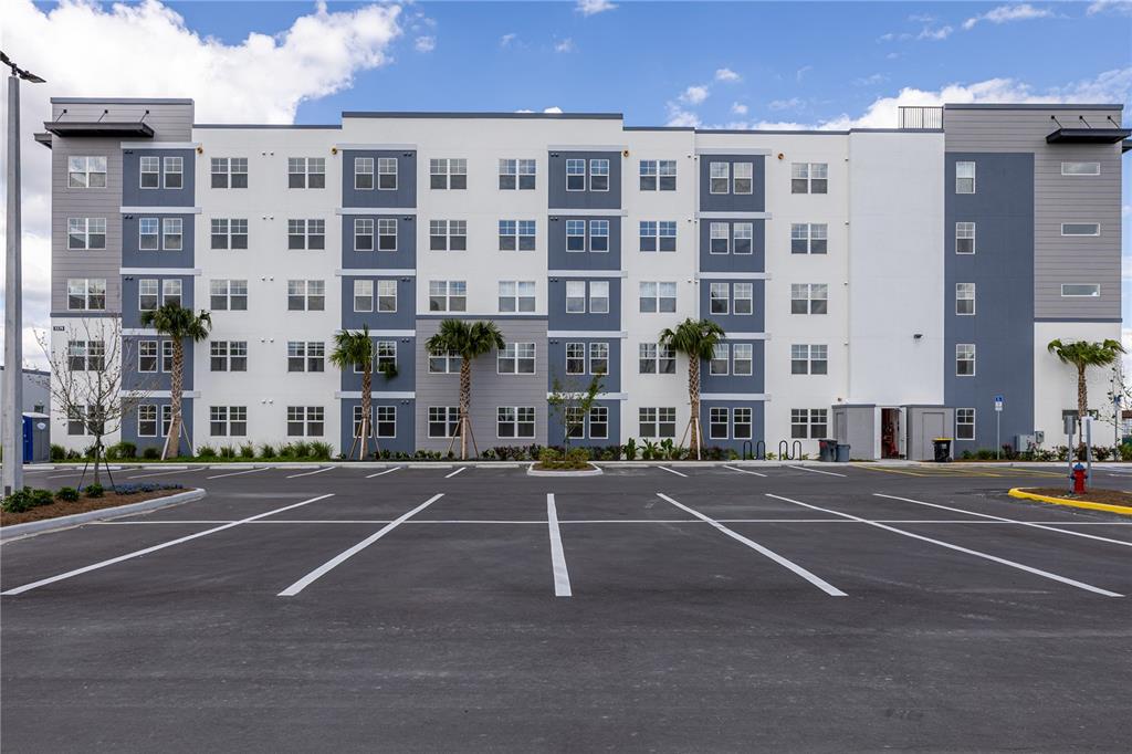 A multi-story apartment building with a parking lot in the foreground under a blue sky — 5579 MILLENIA PARK BOULEVARD UNIT 323, ORLANDO, FL