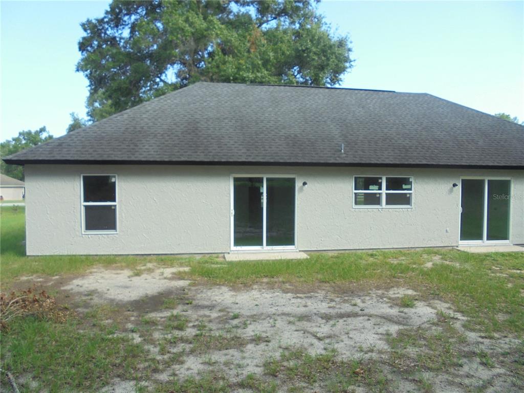 A side view of a white stucco house with a dark shingled roof and lawn — 340 EMERALD ROAD, OCALA, FL
