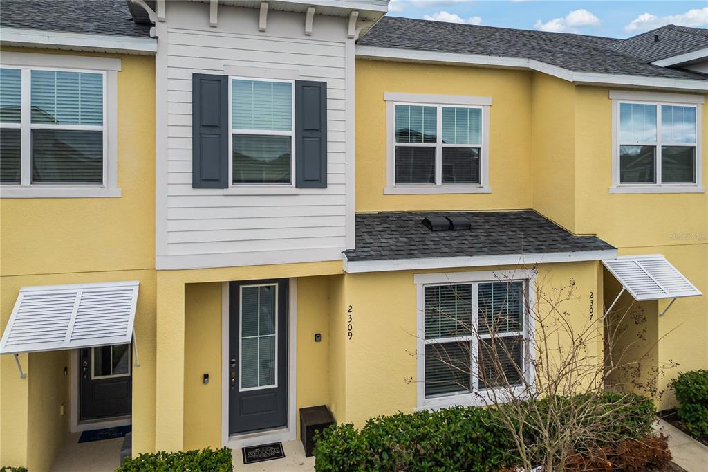 An exterior view of a yellow two-story townhouse with white trim and dark gray shutters — 2309 DISTANT SUN TRAIL, KISSIMMEE, FL