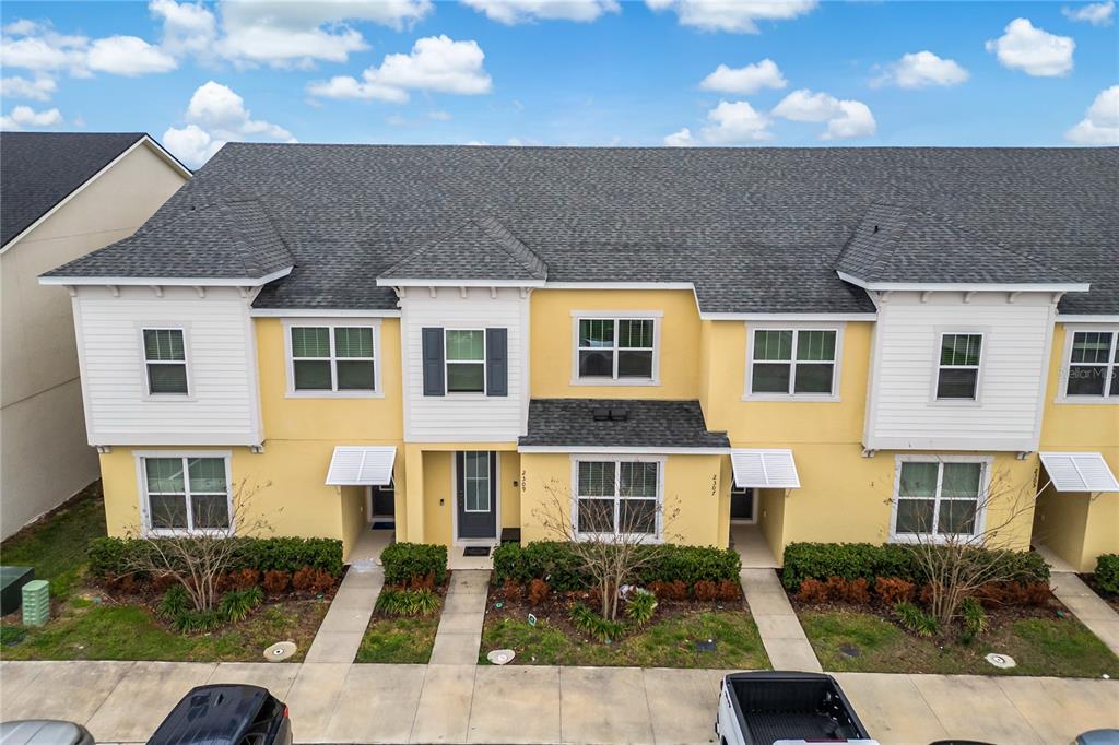 An exterior view of a yellow multi-unit townhouse building with a gray shingled roof — 2309 DISTANT SUN TRAIL, KISSIMMEE, FL