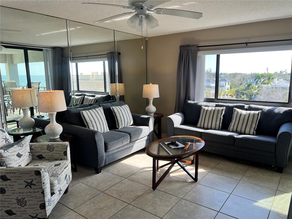 A living room features a dark sofa, a patterned armchair, mirrored walls, and a large window — 1001 POINT OF ROCKS ROAD UNIT 608, SARASOTA, FL