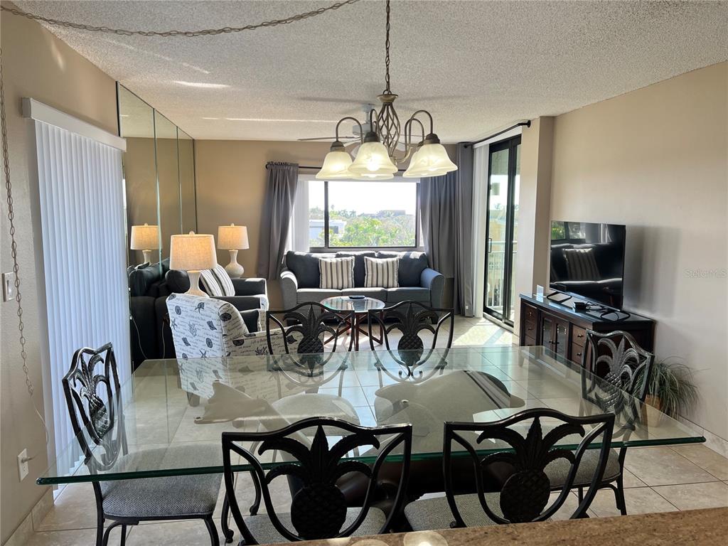 A dining area with a glass table and pineapple-motif chairs overlooks a living room — 1001 POINT OF ROCKS ROAD UNIT 608, SARASOTA, FL