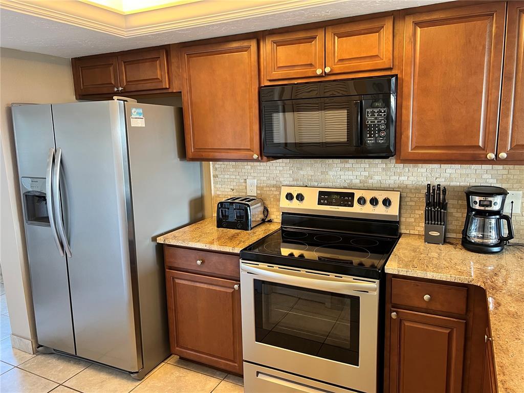 A kitchen features stainless steel appliances, wood cabinets, and granite countertops with a tiled backsplash — 1001 POINT OF ROCKS ROAD UNIT 608, SARASOTA, FL
