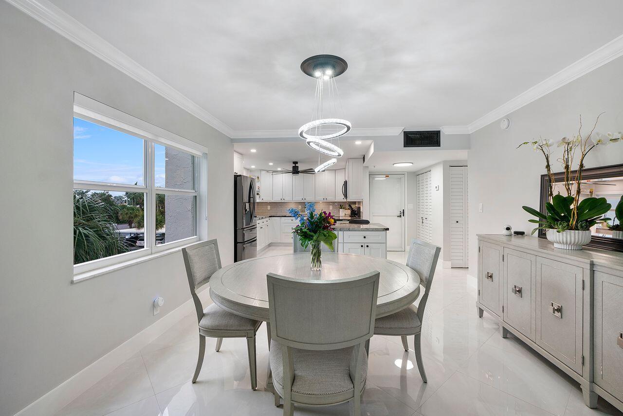 A dining area with a round table and modern chandelier opens into a white kitchen — 3300 S Ocean Boulevard # c, Highland Beach FL 33487, HIGHLAND BEACH, FL