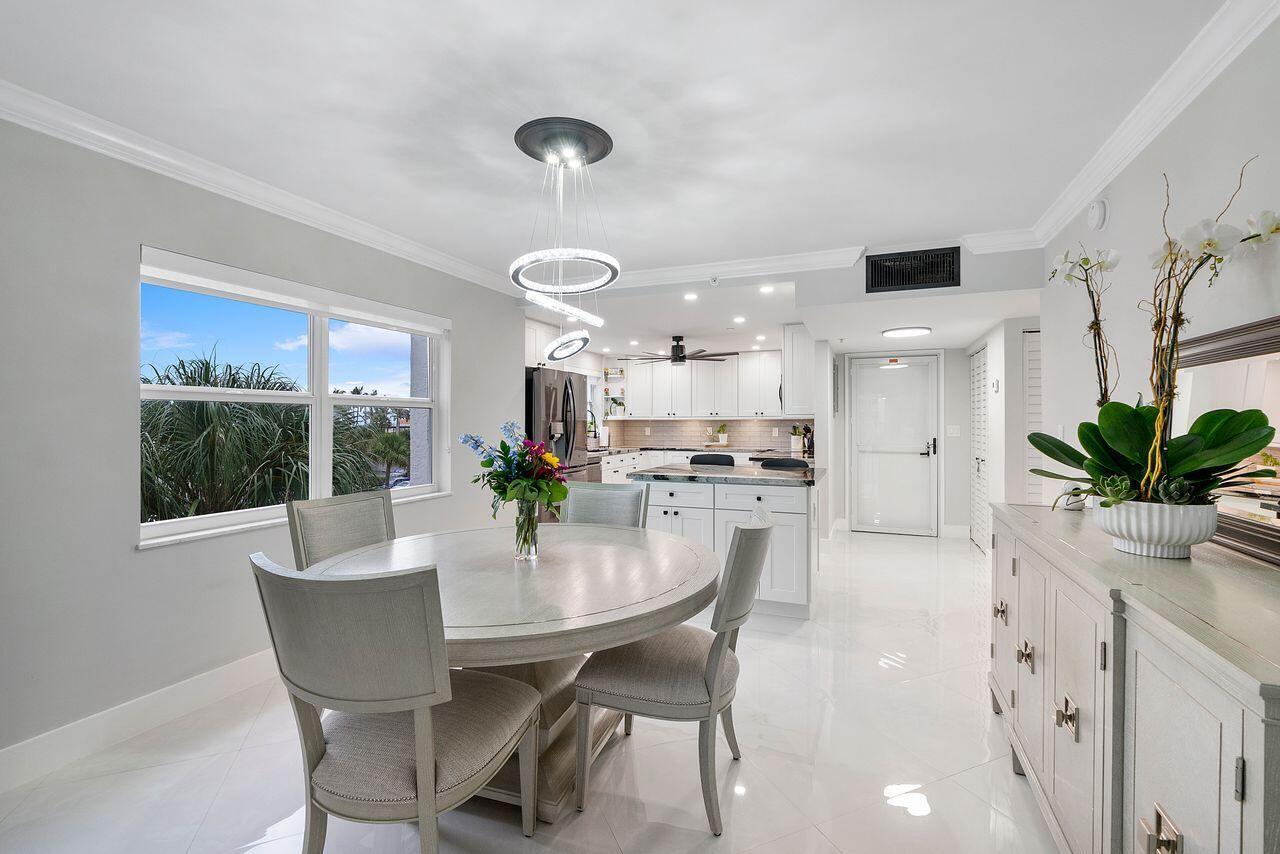 A dining area with a round table, modern chandelier, and an open kitchen with white cabinets — 3300 S Ocean Boulevard # c, Highland Beach FL 33487, HIGHLAND BEACH, FL