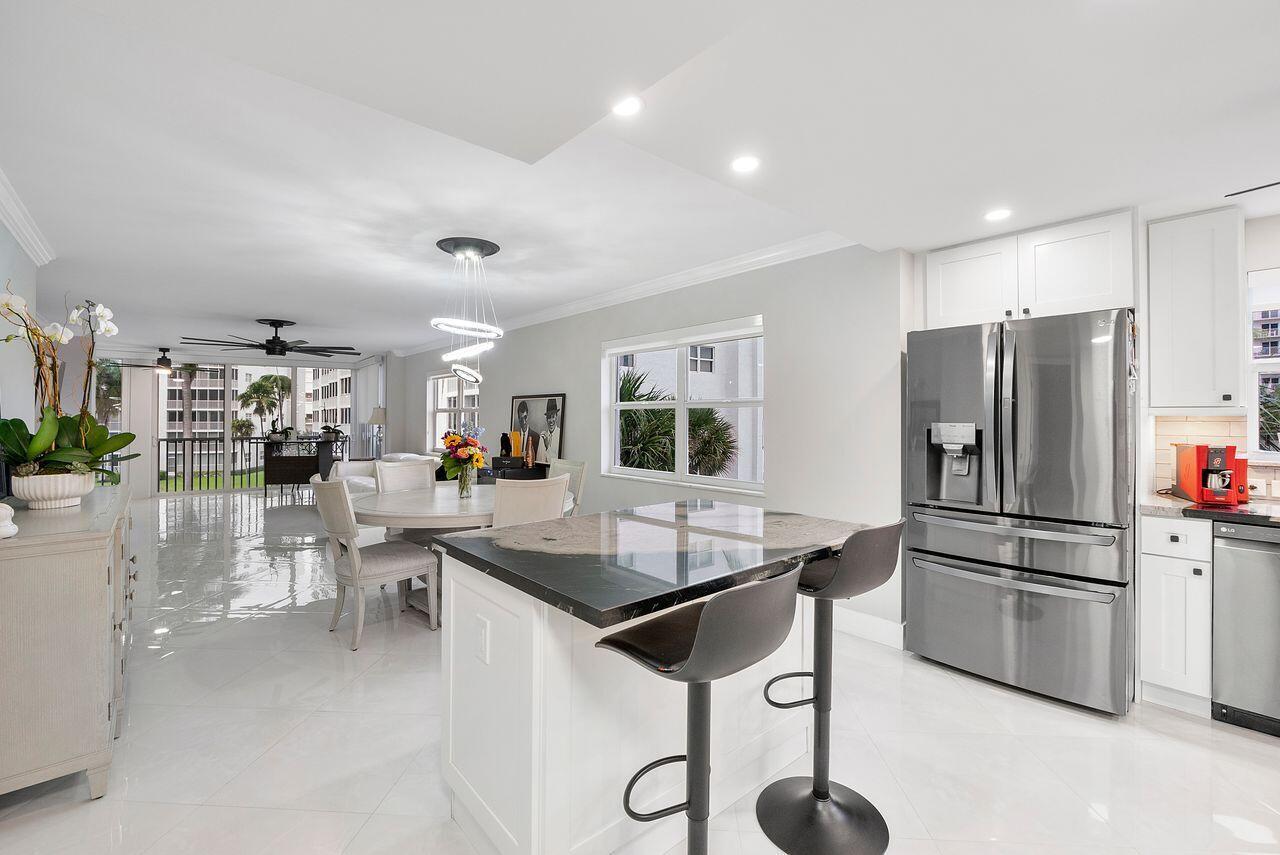 A bright, open-concept kitchen and dining area features white cabinetry, a dark stone island, and tile floors — 3300 S Ocean Boulevard # c, Highland Beach FL 33487, HIGHLAND BEACH, FL