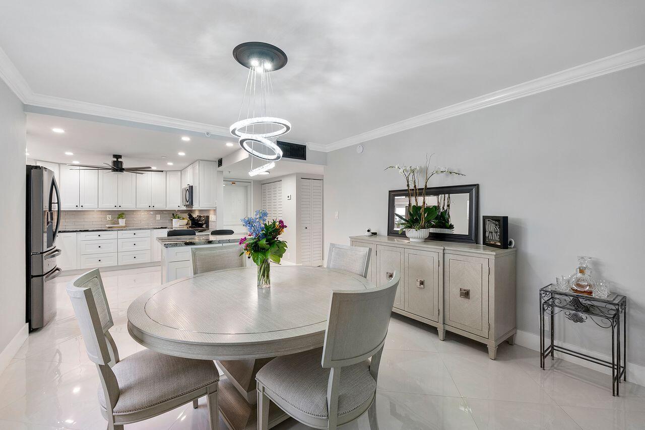 A dining area with a round table, modern chandelier, and an adjacent white kitchen — 3300 S Ocean Boulevard # c, Highland Beach FL 33487, HIGHLAND BEACH, FL