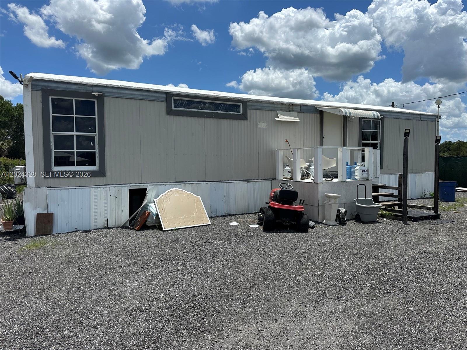 The exterior of a single-wide mobile home features light siding, a small porch, and gravel — 625 N QUEBRADA, Clewiston FL 33440, CLEWISTON, FL
