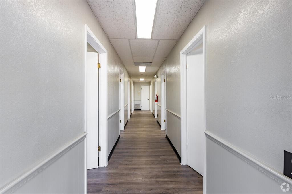 A narrow hallway with light gray walls, white trim, and wood-look flooring leads to a door — 5623 US-19 N HIGHWAY, NEW PORT RICHEY, FL