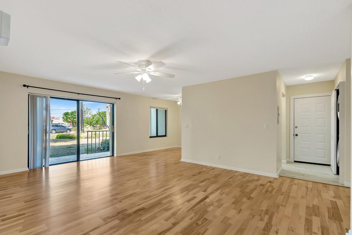 An empty living room features hardwood floors, a ceiling fan, sliding glass doors, and an entryway — 150 Pineview Road # B2, Jupiter FL 33469, JUPITER, FL
