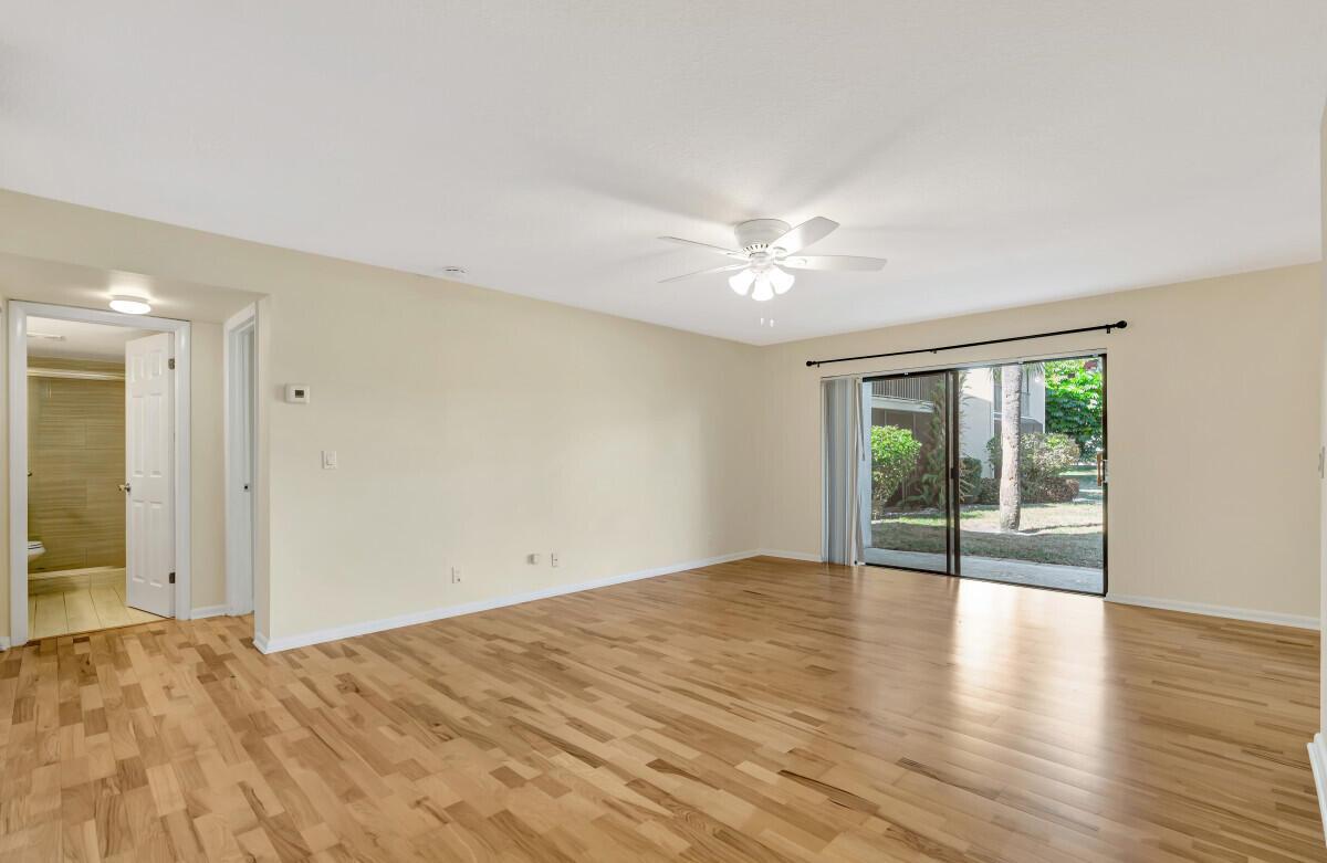 An empty living room with light hardwood floors, a ceiling fan, and sliding glass doors — 150 Pineview Road # B2, Jupiter FL 33469, JUPITER, FL