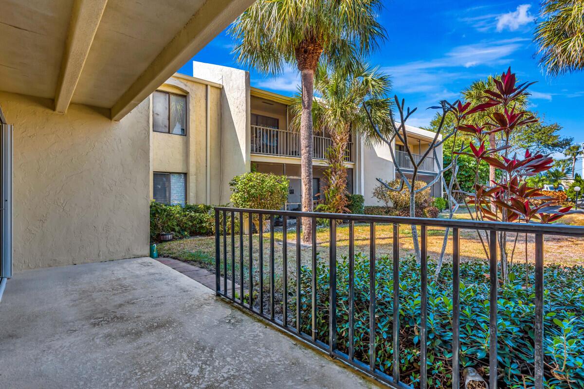 A concrete patio overlooks a grassy courtyard with palm trees and a multi-story apartment building — 150 Pineview Road # B2, Jupiter FL 33469, JUPITER, FL