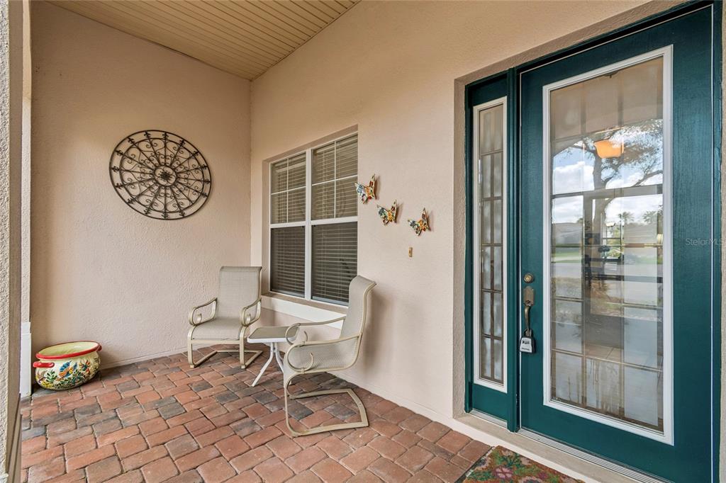 A covered patio features brick pavers, two chairs, a small table, and a teal door — 113 TIVOLI TRACE CT, POINCIANA, FL