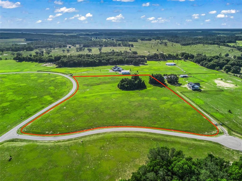An aerial view shows a large, vacant grassy lot outlined in red along a curved road — 0 NE 54TH TERRACE, ANTHONY, FL