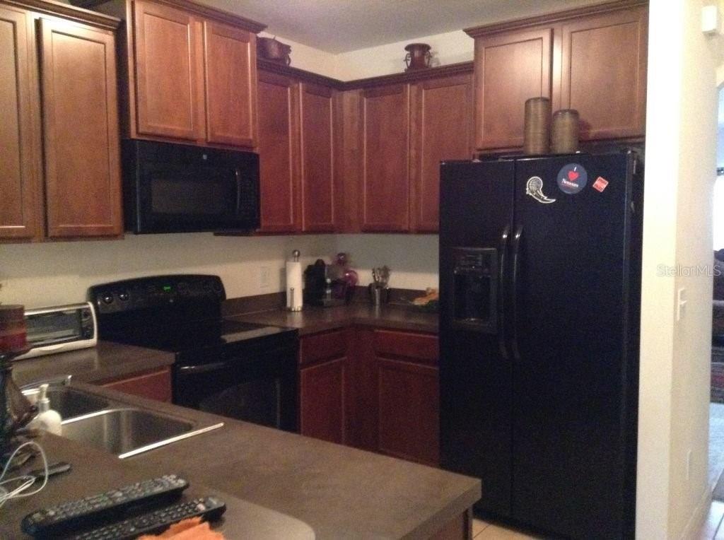 A kitchen features dark wood cabinets, black appliances, and a dark countertop with a sink — 2310 TRILLIUM PARK LANE, SANFORD, FL