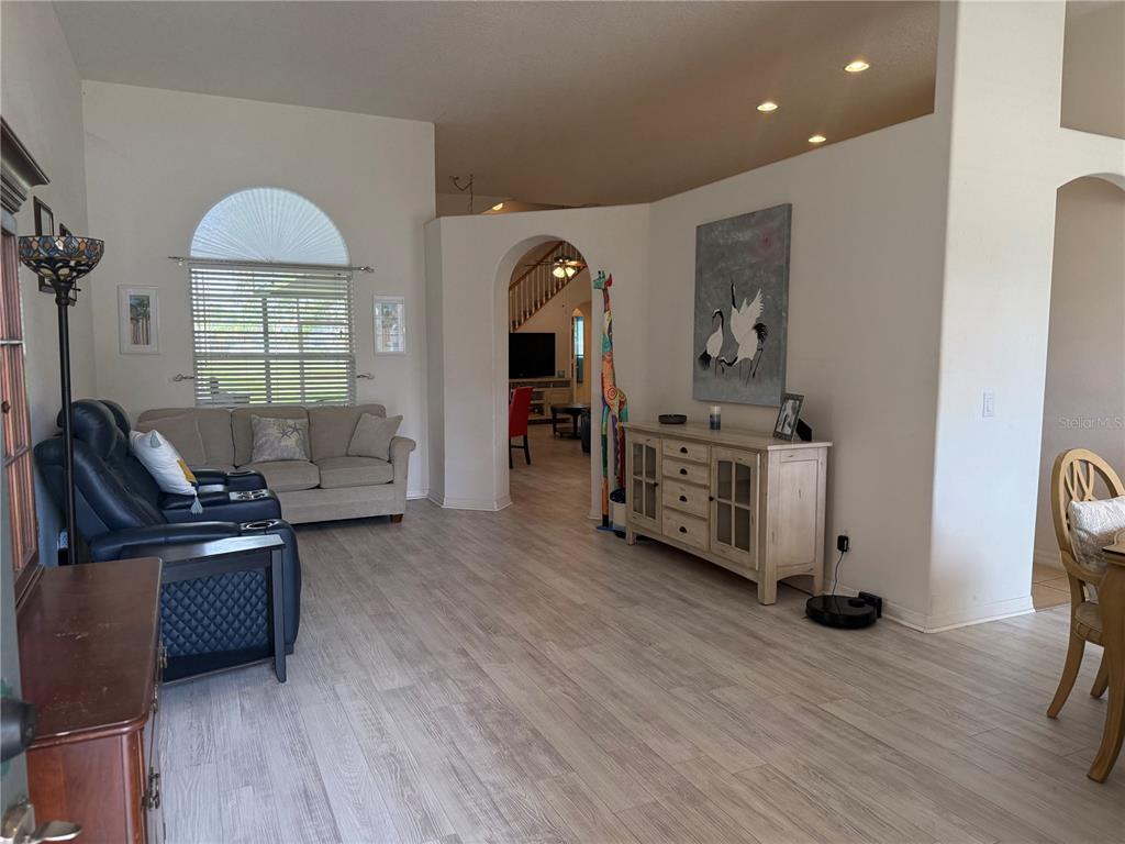 A living room with light wood-look flooring, a beige sofa, and an arched entryway — 1043 CHAMBERLIN TRAIL, ST CLOUD, FL