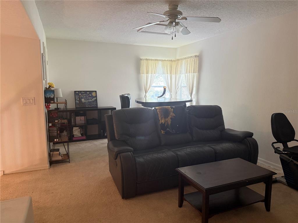 A living room features a dark leather sofa, a coffee table, and a dining area — 1043 CHAMBERLIN TRAIL, ST CLOUD, FL