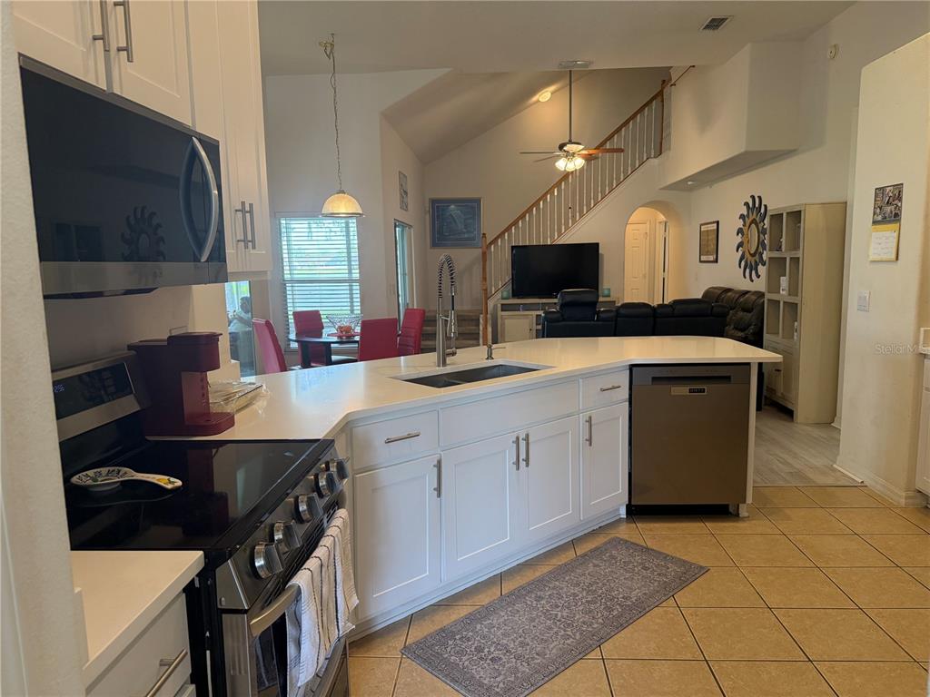 A kitchen with white cabinets, stainless steel appliances, and a quartz island overlooks the living area — 1043 CHAMBERLIN TRAIL, ST CLOUD, FL