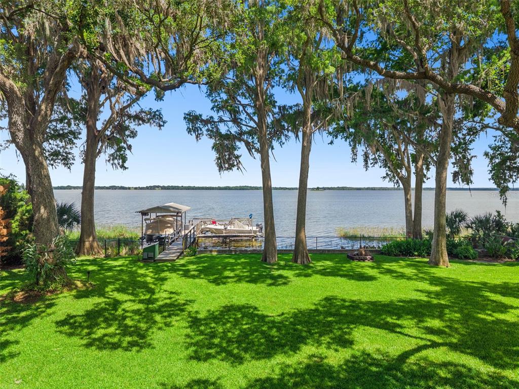 A wooden dock with a boat lift sits on a lake in front of a house — 1000 N LAKESHORE BOULEVARD, HOWEY IN THE HILLS, FL