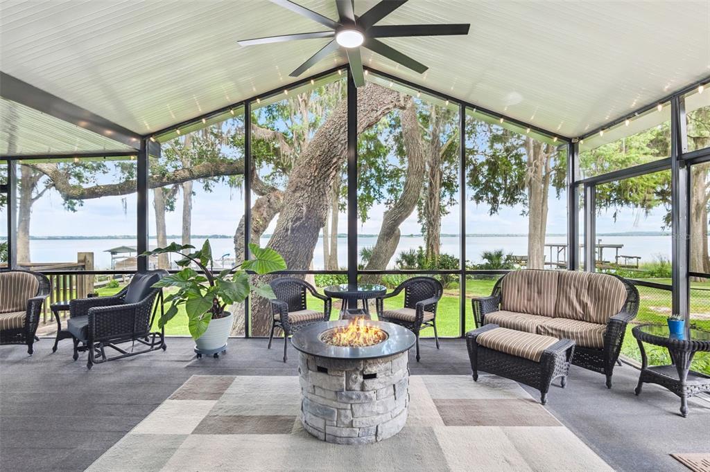 A screened-in porch features a stone fire pit, wicker furniture, and a view of a lake — 1000 N LAKESHORE BOULEVARD, HOWEY IN THE HILLS, FL