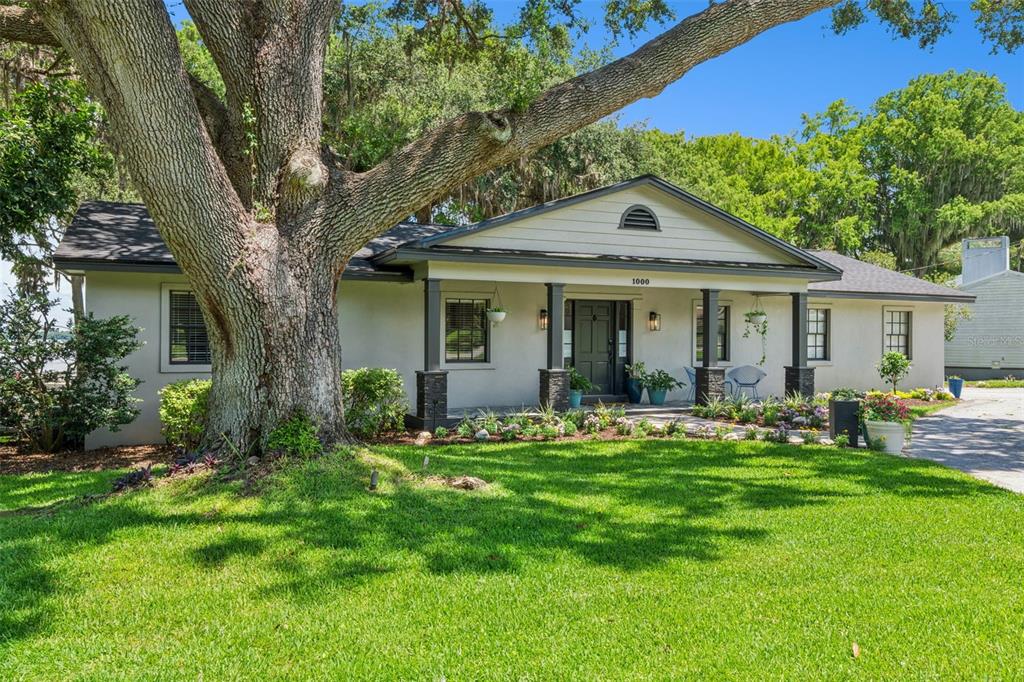 A single-story house with a large oak tree in the front yard and a covered porch — 1000 N LAKESHORE BOULEVARD, HOWEY IN THE HILLS, FL