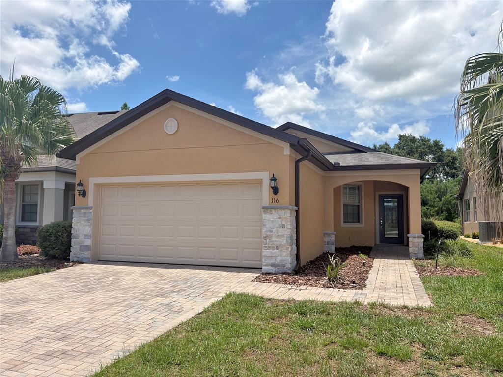 A single-story house with a tan stucco exterior, stone accents, and a paved driveway — 116 LA CRESTA COURT, DAVENPORT, FL