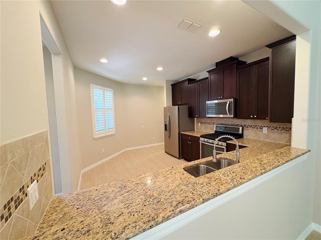 A kitchen features dark wood cabinets, granite countertops, stainless steel appliances, and a breakfast nook — 116 LA CRESTA COURT, DAVENPORT, FL
