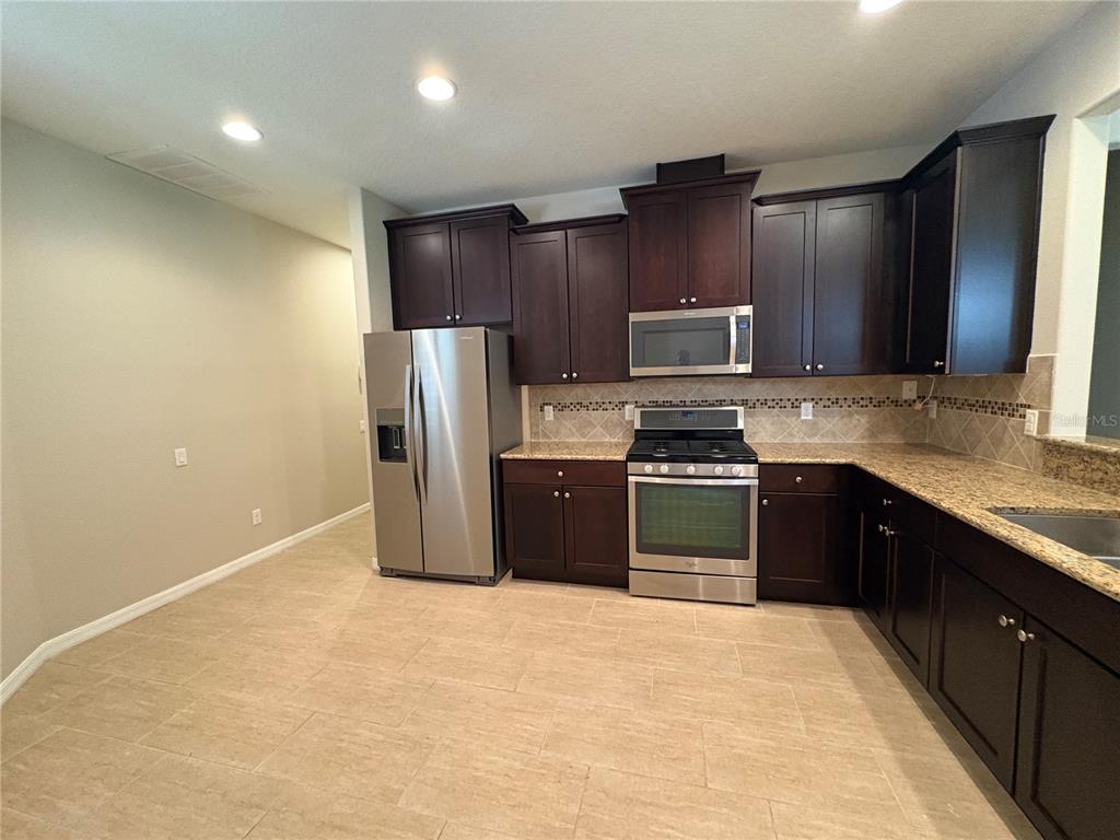 A kitchen features dark wood cabinets, stainless steel appliances, and granite countertops over tile flooring — 116 LA CRESTA COURT, DAVENPORT, FL