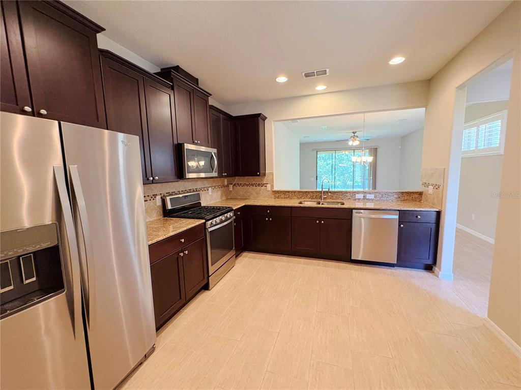 A kitchen features dark wood cabinets, granite countertops, stainless steel appliances, and tile flooring — 116 LA CRESTA COURT, DAVENPORT, FL