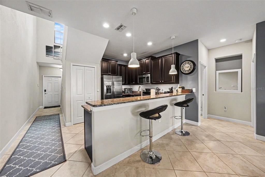 A kitchen features dark wood cabinets, granite countertops, a breakfast bar, and tile flooring — 28504 TRANQUIL LAKE CIRCLE, WESLEY CHAPEL, FL
