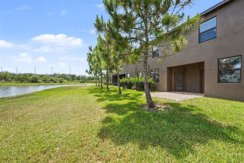 A two-story townhouse exterior with a small patio, lawn, and trees beside a pond — 28504 TRANQUIL LAKE CIRCLE, WESLEY CHAPEL, FL