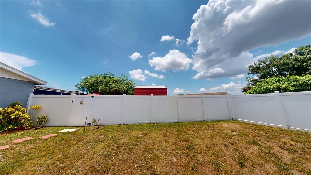 A backyard features a white vinyl privacy fence, a red shed, and a grassy lawn — 1215 COOLMONT DRIVE, BRANDON, FL