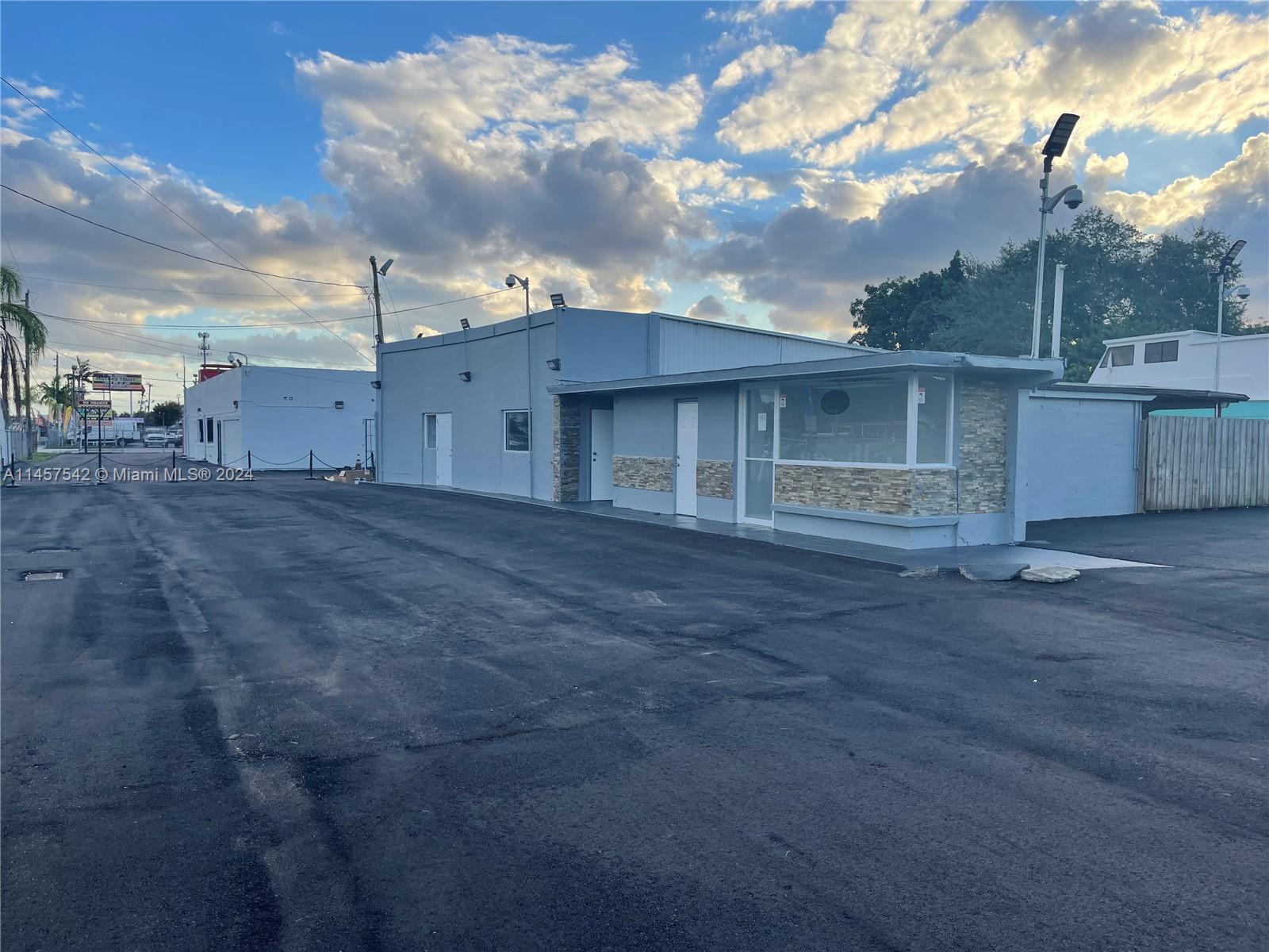 A gray commercial building with stone accents sits on a large, paved asphalt parking lot — 9800 NW 27th Ave, Miami FL 33147, MIAMI, FL