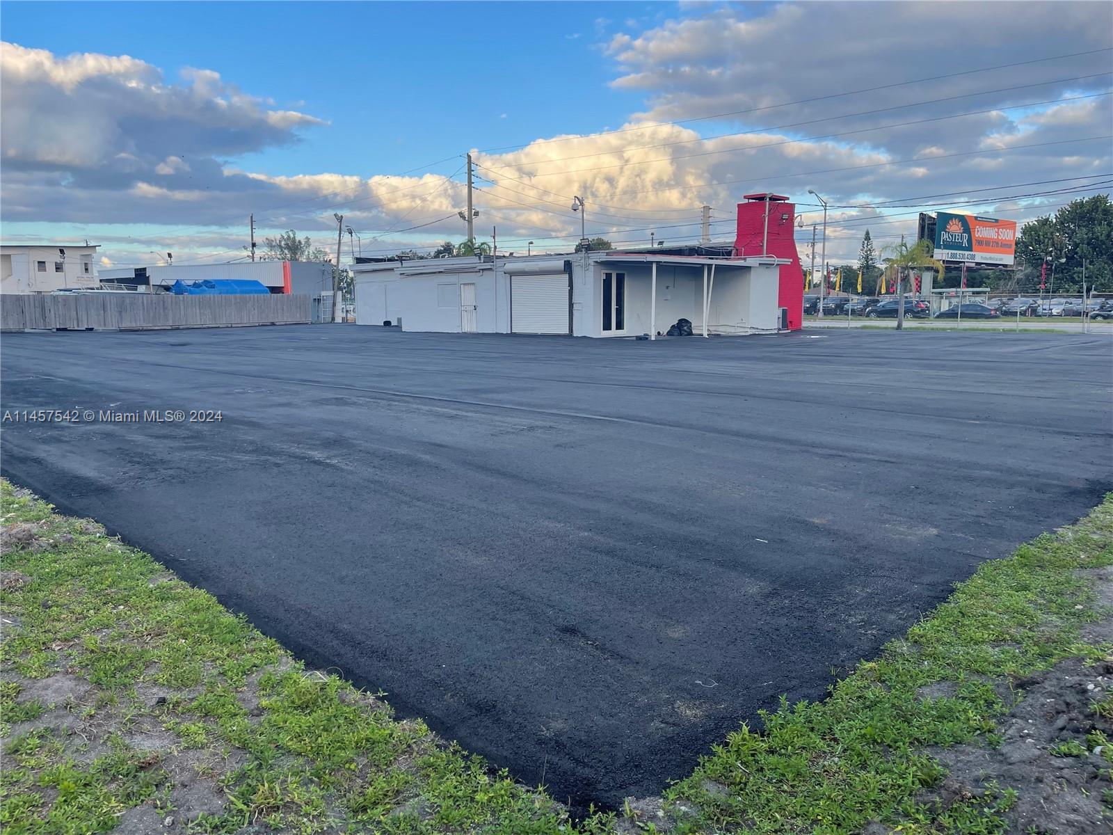A commercial building with a red chimney stands behind a large, newly paved asphalt lot — 9800 NW 27th Ave, Miami FL 33147, MIAMI, FL