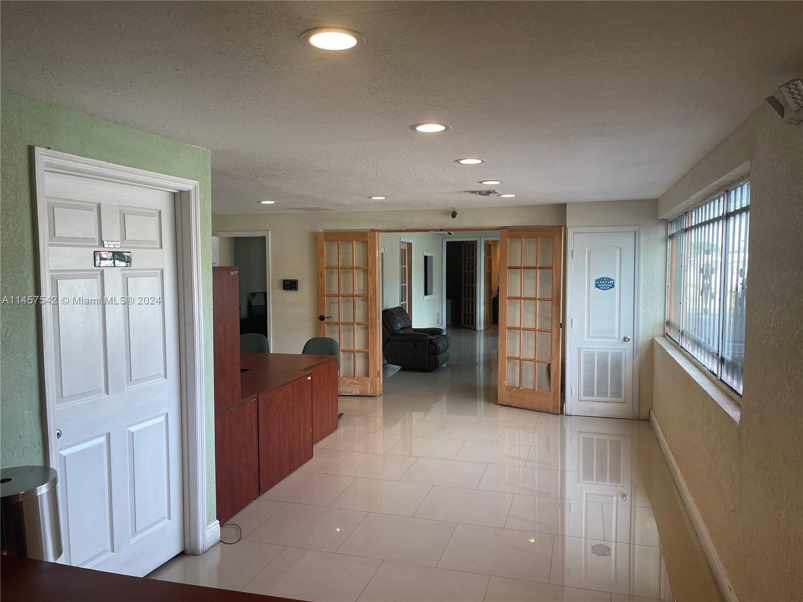 An office interior features tile flooring, recessed lighting, wooden French doors, and a reception desk — 9800 NW 27th Ave, Miami FL 33147, MIAMI, FL