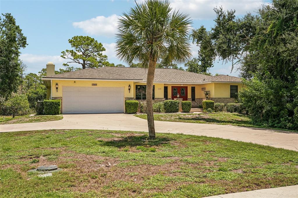 A single-story yellow house with a two-car garage and a palm tree in the yard — 1305 SORRENTO WOODS BOULEVARD, NOKOMIS, FL