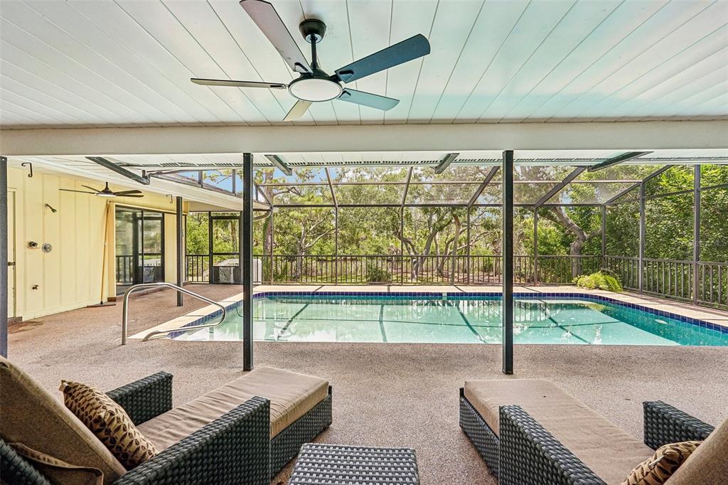 A covered patio with a ceiling fan overlooks a screened-in swimming pool and wooded yard — 1305 SORRENTO WOODS BOULEVARD, NOKOMIS, FL