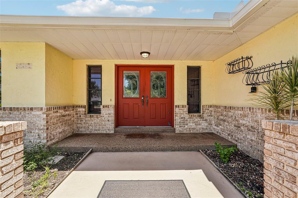 The exterior view shows a house entrance with a red double door and brick siding — 1305 SORRENTO WOODS BOULEVARD, NOKOMIS, FL