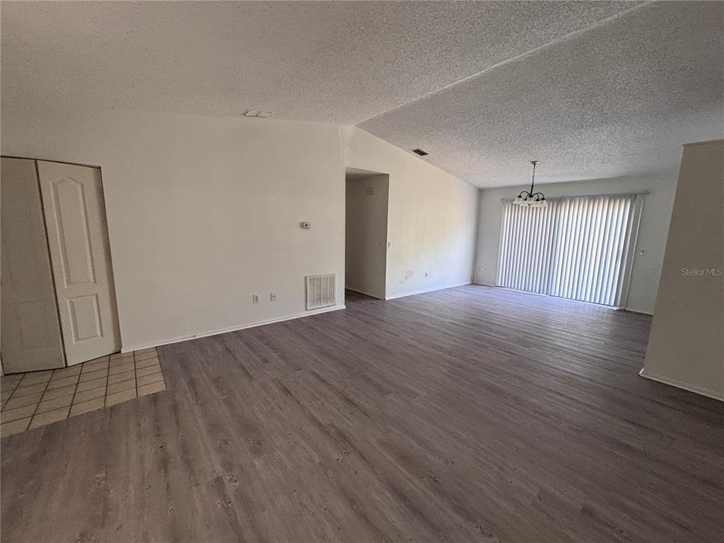 An open-concept living area features light gray wood-look flooring, white walls, and sliding glass doors — 1028 HICKORY ROAD, OCALA, FL