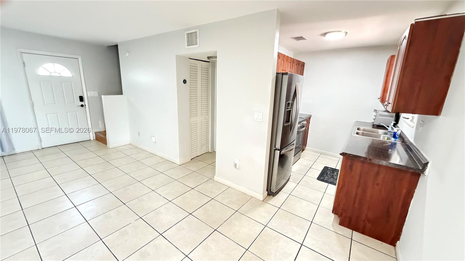A kitchen with tile floors, wooden cabinets, and stainless steel appliances opens to a living area — 11249 SW 33rd Cir Pl, Miami FL 33165, MIAMI, FL