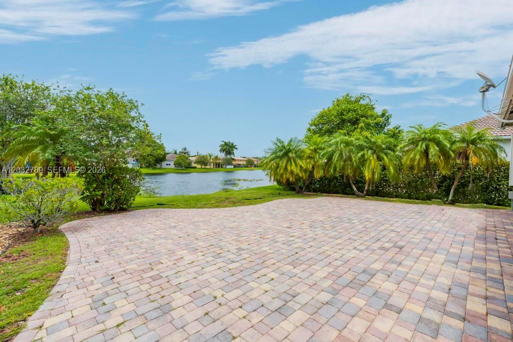 A paved patio overlooks a lake surrounded by palm trees and residential homes — 19301 Seneca Ave, Weston FL 33332, WESTON, FL