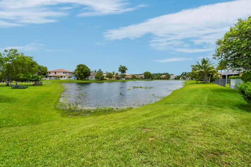 A grassy lawn slopes down to a pond surrounded by residential houses and palm trees — 19301 Seneca Ave, Weston FL 33332, WESTON, FL