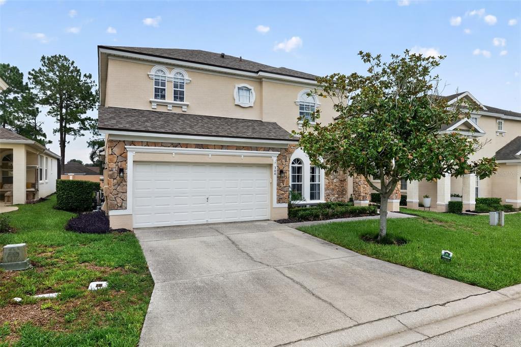 A two-story suburban house with a tan stucco exterior, stone accents, and a two-car garage — 304 CALABAY PARC BOULEVARD, DAVENPORT, FL