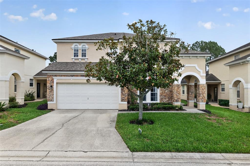 A two-story house with a beige stucco exterior, stone accents, and a two-car garage — 304 CALABAY PARC BOULEVARD, DAVENPORT, FL