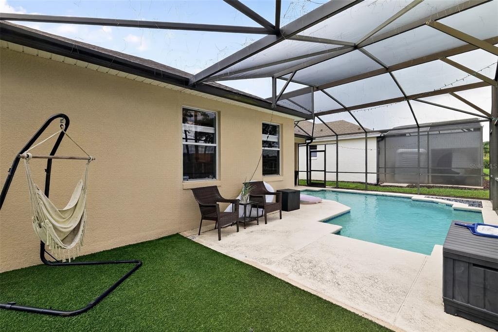 A screened-in patio features a swimming pool, artificial turf, and a hanging hammock chair — 304 CALABAY PARC BOULEVARD, DAVENPORT, FL