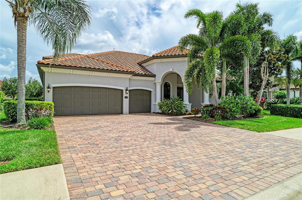 A single-story house with a paver driveway, a three-car garage, and a tiled roof — 13304 BRIDGEPORT CROSSING, BRADENTON, FL