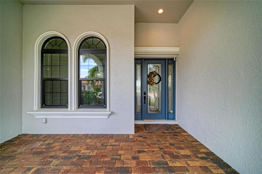 A front entryway features a blue door with glass panels, arched windows, and brick pavers — 13304 BRIDGEPORT CROSSING, BRADENTON, FL